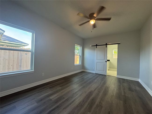 Unfurnished bedroom featuring a barn door, dark wood finished floors, ensuite bathroom, and ceiling fan | Image 15