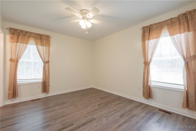 Empty room with a ceiling fan, wood finished floors, a wealth of natural light, and visible vents | Image 24