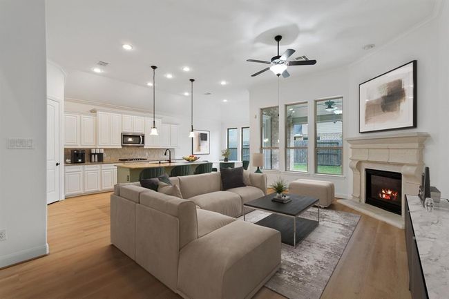 The inviting living room seamlessly flows into the kitchen, featuring a stylish ceiling fan, multiple windows for abundant natural light, and a cozy gas log fireplace—perfect for relaxation and entertaining! *Virtually Staged* | Image 6