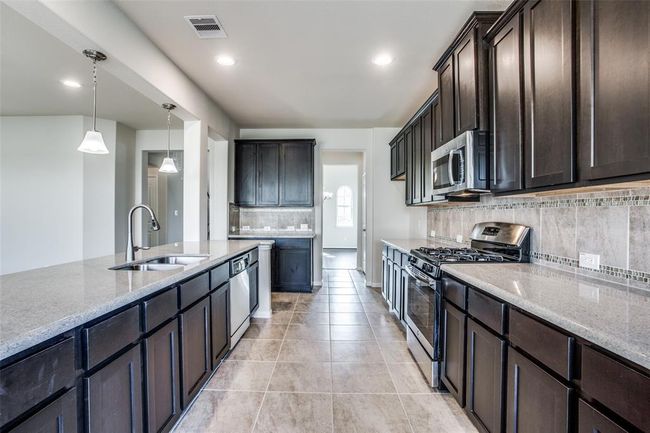 Modern kitchen with dark cabinets, stainless steel appliances, granite countertops, and pendant lighting over an island. | Image 11