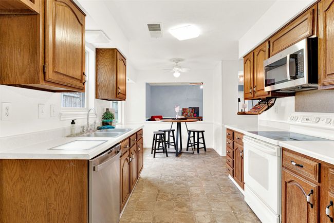 Kitchen with appliances with stainless steel finishes, brown cabinetry, a ceiling fan, stone finish floors, and light countertops | Image 32