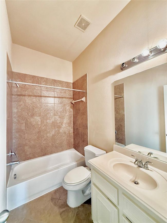 This second bathroom features a clean design with a tiled shower-tub combo, a white vanity with a sink, and a large mirror under bright lighting. | Image 8