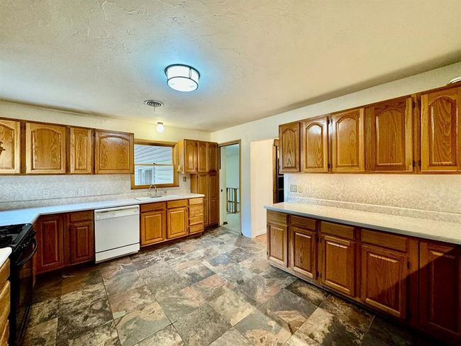 Kitchen with white dishwasher, black range, brown cabinets, light countertops, and dark stone finish flooring | Image 7