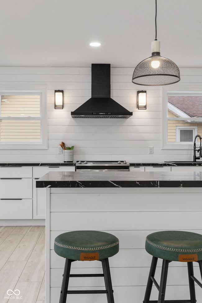 kitchen featuring a breakfast bar area, wall chimney exhaust hood, a sink, and white cabinetry | Image 21