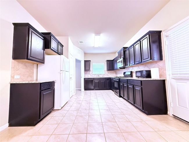 Kitchen featuring backsplash, black appliances, light stone countertops, and light tile patterned floors | Image 5