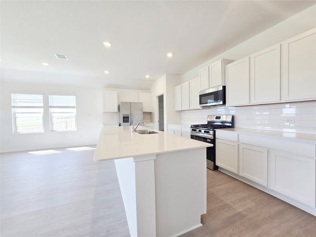 Kitchen featuring stainless steel appliances, a sink, an island with sink, backsplash, and light wood-style flooring | Image 24