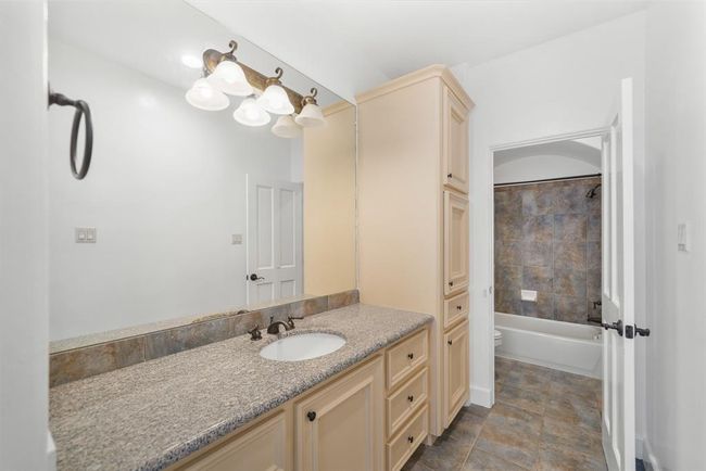 The private dressing area with a built-in linen storage area and clothes hamper includes painted cabinets supporting a granite counter top with a tiled back splash, wall mounted mirror & lighting & tile flooring. Access to the private water closet is shown in the background. | Image 39