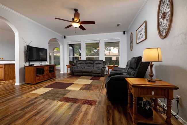 Living room with wood finished floors, a ceiling fan, arched walkways, crown molding, and baseboards | Image 9