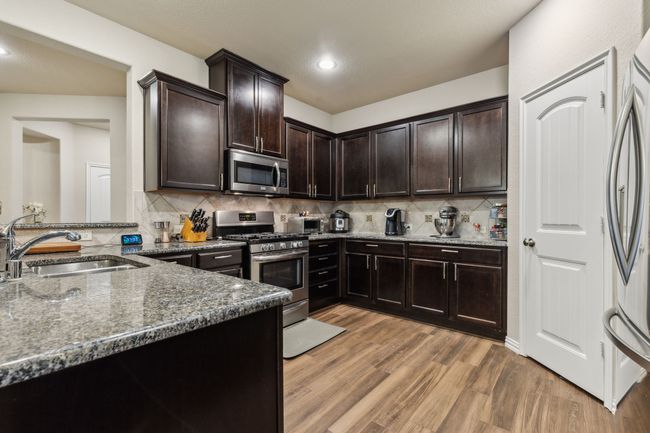 Kitchen featuring appliances with stainless steel finishes, a sink, dark stone counters, light wood finished floors, and dark brown cabinets | Image 7