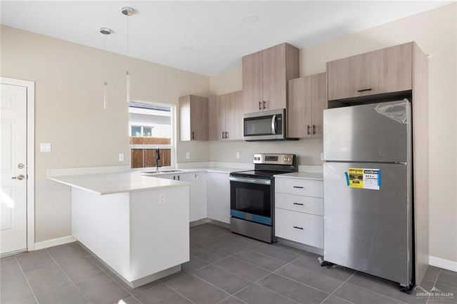 Kitchen with a peninsula, a sink, dark tile patterned flooring, stainless steel appliances, and light countertops | Image 12