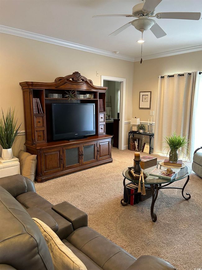 Carpeted living area featuring a ceiling fan and crown molding | Image 8
