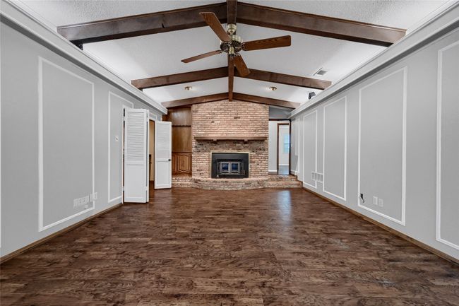 Unfurnished living room with a fireplace, a ceiling fan, lofted ceiling with beams, and dark wood finished floors | Image 11