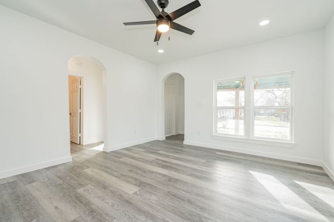 Empty room with light wood-style flooring, arched walkways, baseboards, and recessed lighting | Image 4