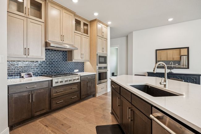 Kitchen with stainless steel appliances, a sink, under cabinet range hood, light countertops, and light wood-style flooring | Image 21