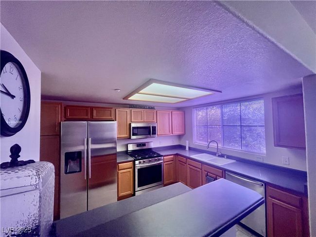 Kitchen with a textured ceiling, dark countertops, a sink, and stainless steel appliances | Image 12