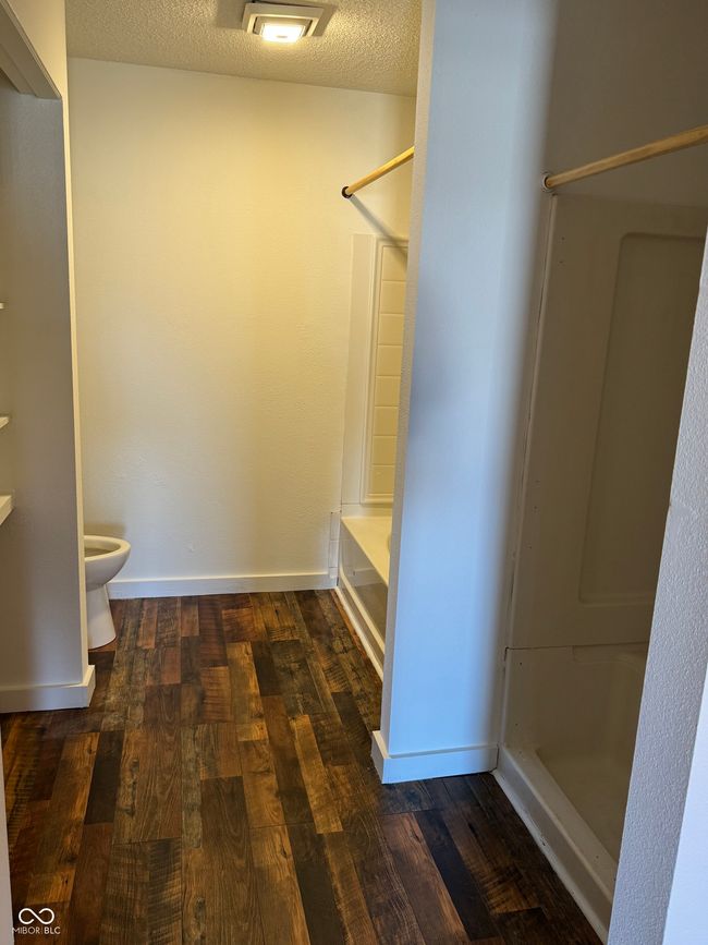 interior space featuring baseboards, separate tub and shower co wood finished floors, and a textured ceiling | Image 13