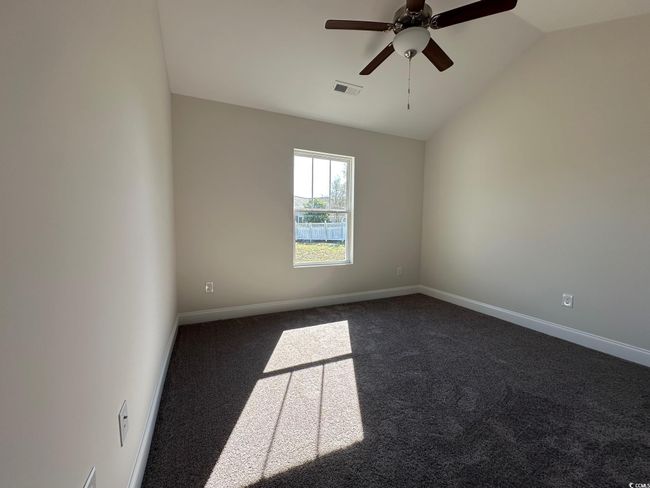 Empty room with baseboards, visible vents, ceiling fan, vaulted ceiling, and dark colored carpet | Image 15