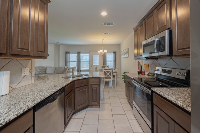 Kitchen featuring appliances with stainless steel finishes, light tile patterned floors, decorative backsplash, a chandelier, and dark brown cabinetry | Image 18
