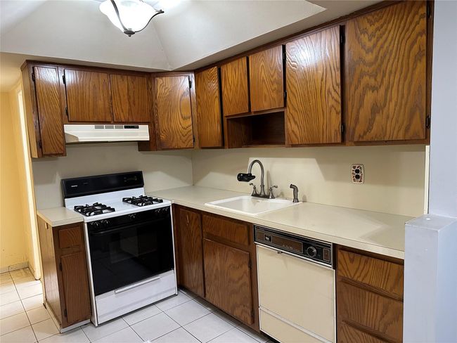 Kitchen with under cabinet range hood, a sink, light countertops, dishwasher, and gas range oven | Image 10