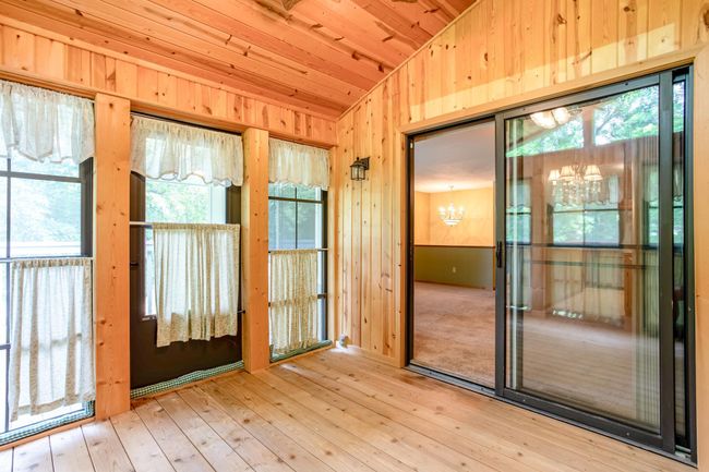 Seamless flow from the main living area into the sun-drenched 3-season porch, framed with warm pine finishes and expansive windows. | Image 15