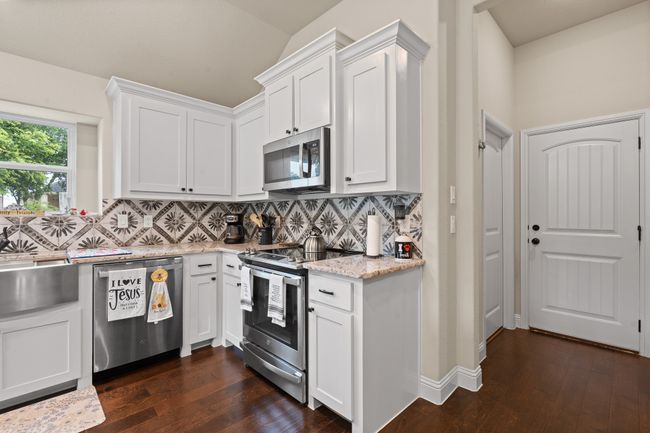 Kitchen with stainless steel appliances, backsplash, dark wood-style floors, white cabinetry, and lofted ceiling | Image 9
