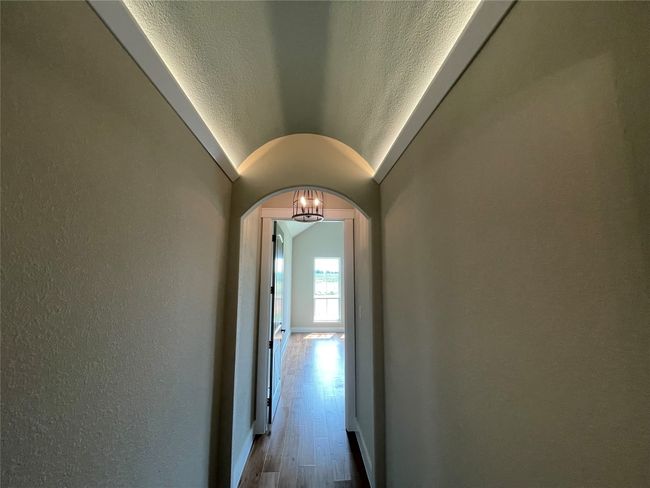 Corridor featuring arched walkways, a textured wall, wood finished floors, and lofted ceiling | Image 29