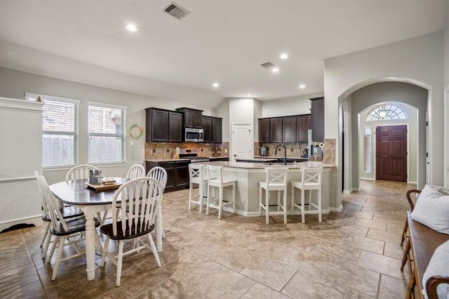 This view showcases how seamlessly the kitchen, dining, and entryway connect—creating a space that’s as functional as it is welcoming. Picture mornings at the breakfast bar, natural light pouring in through the dining windows, and everyday moments unfolding effortlessly in a layout designed for easy living. | Image 12