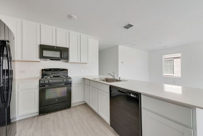 Kitchen featuring black appliances, light countertops, light wood finished floors, a peninsula, and white cabinets | Image 13