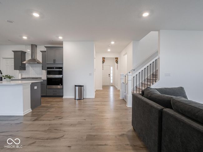 kitchen featuring light wood-style floors, wall chimney range hood, gray cabinets, stainless steel appliances, and open floor plan | Image 9