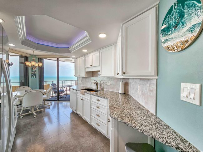 Kitchen with a chandelier, a tray ceiling, backsplash, light stone counters, and recessed lighting | Image 17