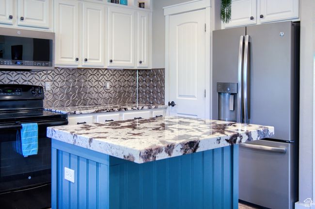 Kitchen with white cabinets, stainless steel appliances, light stone countertops, and tasteful backsplash | Image 9