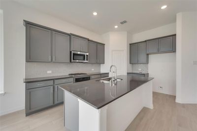 Kitchen featuring decorative backsplash, gray cabinetry, sink, appliances with stainless steel finishes, and a center island with sink | Image 2