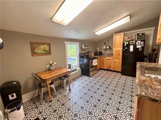 Kitchen featuring stainless steel range with electric stovetop, freestanding refrigerator, vaulted ceiling, a textured ceiling, and a sink | Image 5