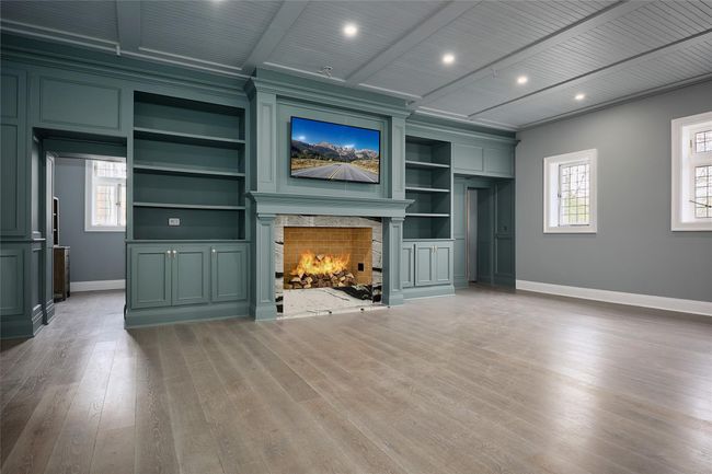 Unfurnished living room with baseboards, wood finished floors, built in features, and a warm lit fireplace | Image 7