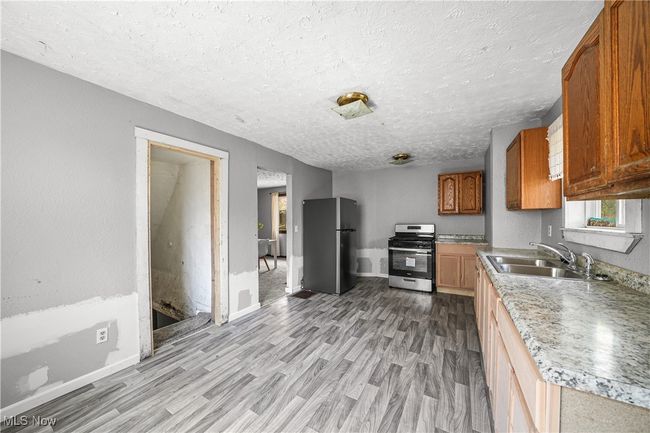 Kitchen featuring a textured ceiling, stainless steel gas range, freestanding refrigerator, light wood-style floors, and brown cabinets | Image 5