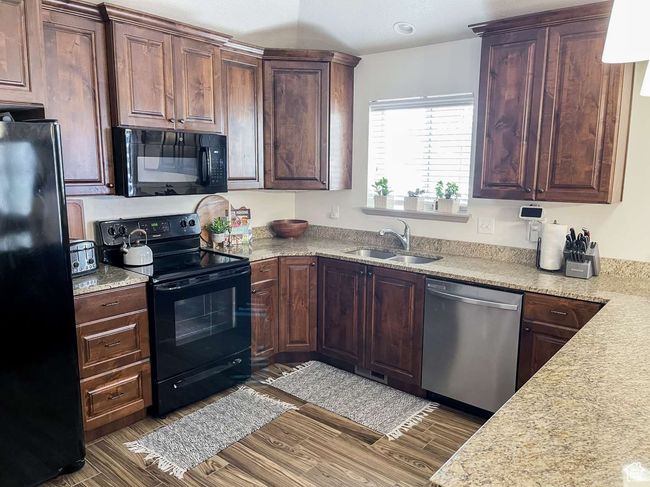 Kitchen with black appliances, a sink, wood finished floors, and dark brown cabinets | Image 15
