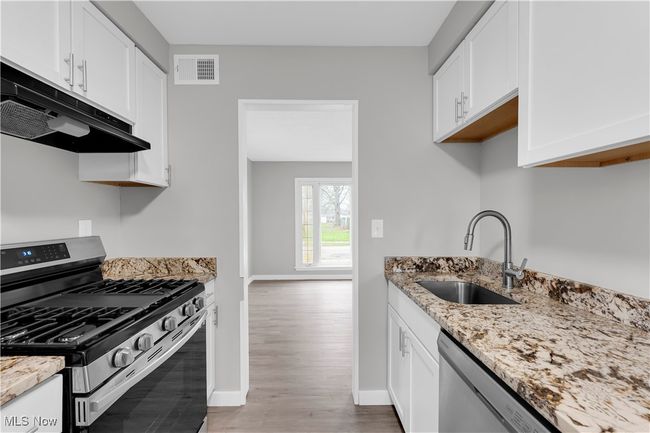 Kitchen with light stone counters, stainless steel appliances, under cabinet range hood, a sink, and visible vents | Image 10