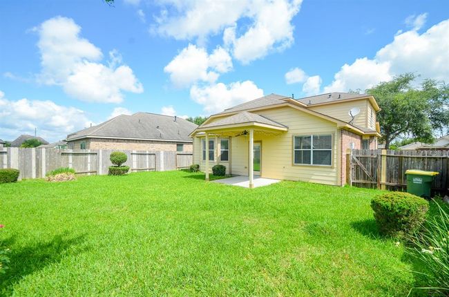 This photo showcases a charming backyard with a spacious, well-maintained lawn, bordered by a wooden fence. The house features beige siding with a covered patio, perfect for outdoor relaxation. The surrounding landscape includes neatly trimmed shrubs and clear blue skies, creating a serene atmosphere. | Image 31