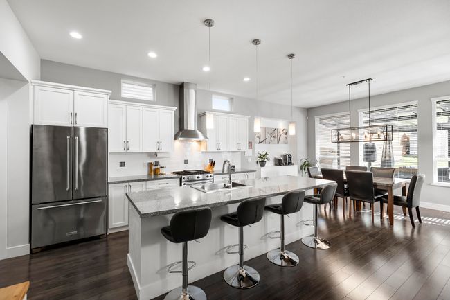 Kitchen with wall chimney range hood, decorative backsplash, stainless steel appliances, white cabinetry, and a sink | Image 8