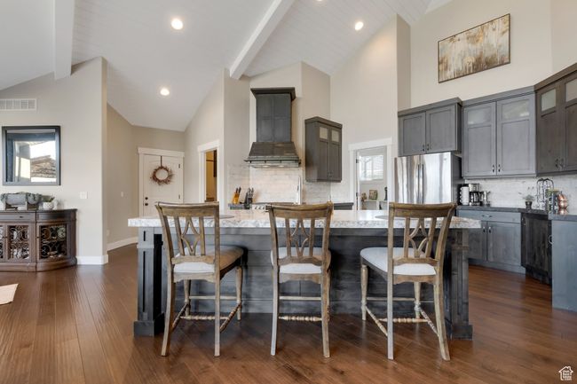 Kitchen with freestanding refrigerator, an island with sink, visible vents, custom exhaust hood, and gray cabinetry | Image 12