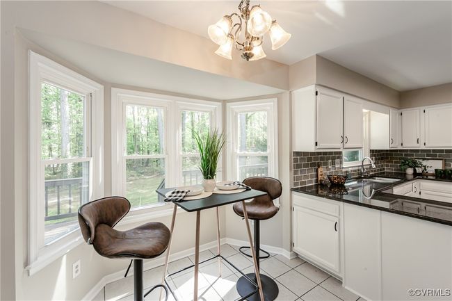 Kitchen with white cabinets, a sink, tasteful backsplash, dark countertops, and an inviting chandelier | Image 21