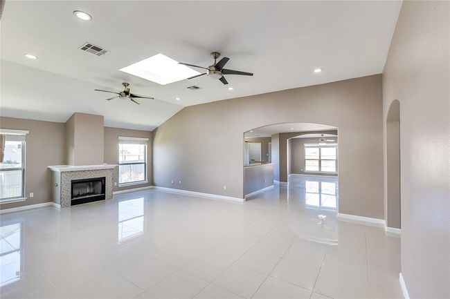 Unfurnished living room featuring a ceiling fan, arched walkways, lofted ceiling, a tile fireplace, and light tile patterned floors | Image 5