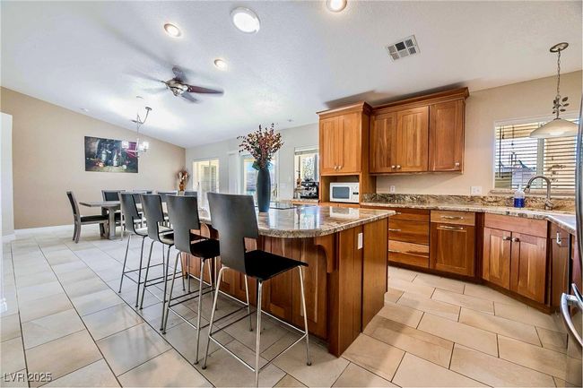 Kitchen with white microwave, visible vents, a sink, a kitchen breakfast bar, and brown cabinets | Image 10