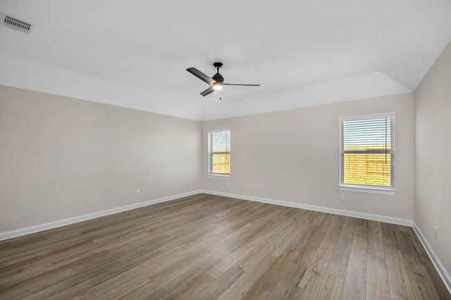Step into luxury in the primary bedroom, where vinyl plank flooring and a ceiling fan combine to create a haven of comfort and style. Sunlight streams through the windows, bathing the space in natural light and offering views of the tranquil surroundings. A doorway leads to the en-suite bathroom, providing a private sanctuary for relaxation and self-indulgence. | Image 5