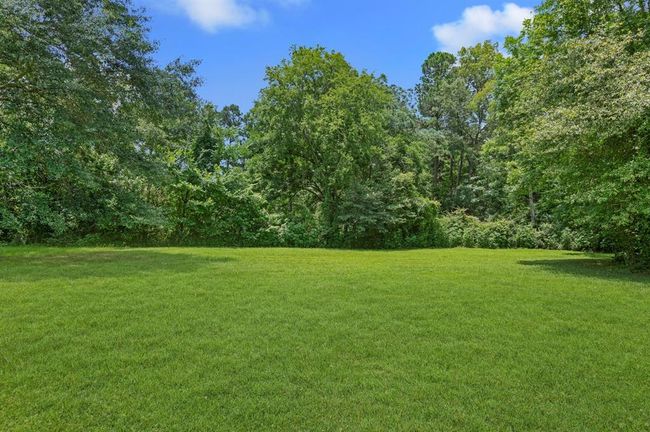 This photo shows a spacious, green lawn surrounded by lush trees, providing a serene and private outdoor space. | Image 23
