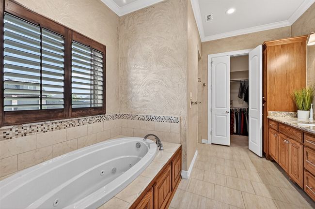 Full bathroom featuring a whirlpool tub, vanity, crown molding, tile patterned flooring, and a spacious closet | Image 26