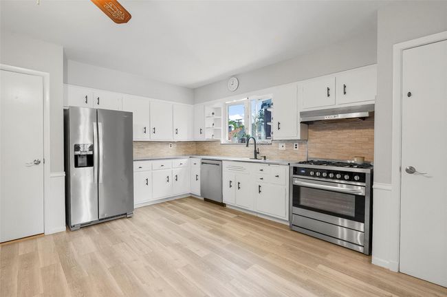 Kitchen with appliances with stainless steel finishes, under cabinet range hood, light wood-style flooring, decorative backsplash, and light countertops | Image 8