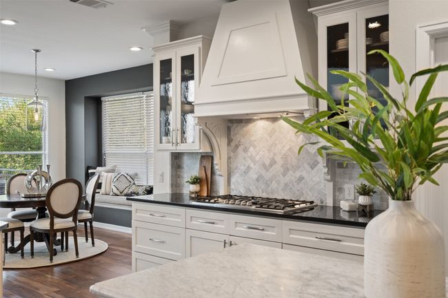 Kitchen featuring white cabinetry, dark wood-style floors, stainless steel gas stovetop, glass insert cabinets, and custom exhaust hood | Image 5