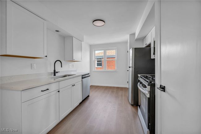 Kitchen featuring range with gas stovetop, light wood-style flooring, white cabinets, stainless steel dishwasher, and a sink | Image 11