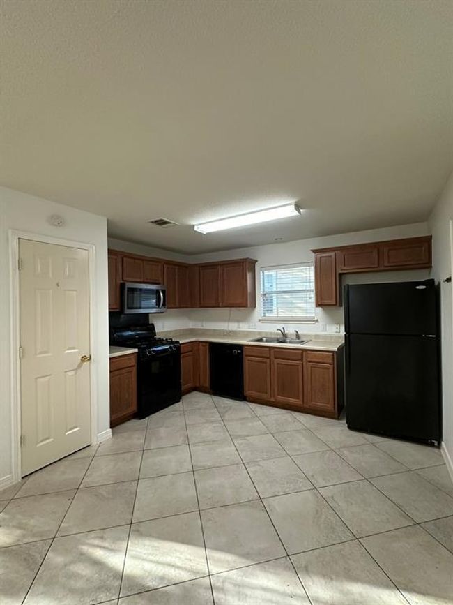 Kitchen with black appliances, light countertops, light tile patterned flooring, and brown cabinets | Image 6